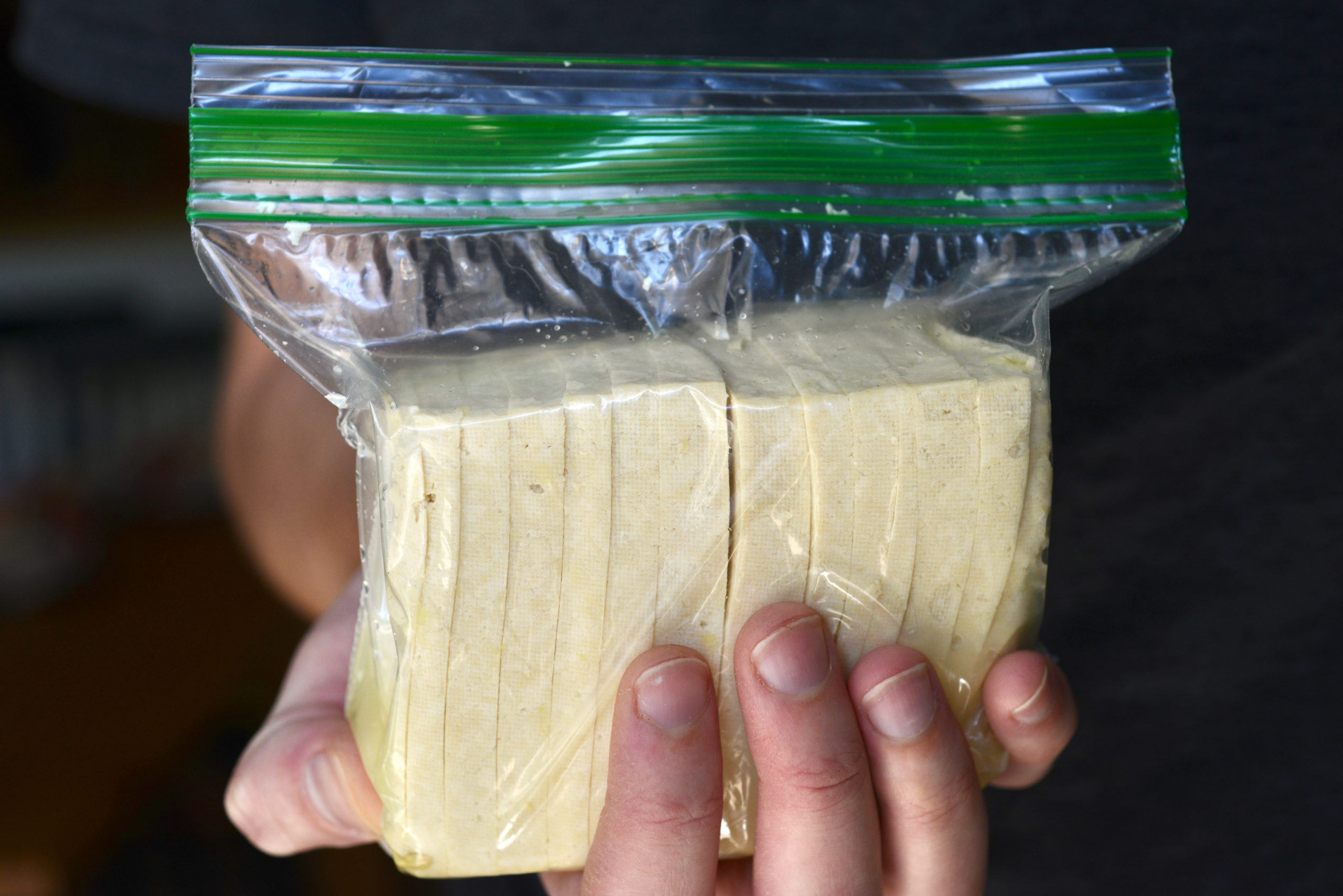 hand holding marinating vegan mozzarella in plastic bag
