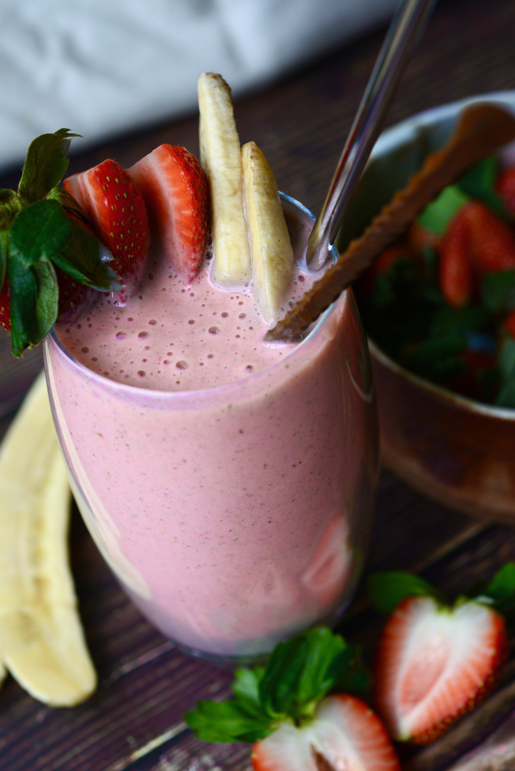 3-ingredient strawberry banana smoothie, angled shot of smoothie in glass with fruit garnishes, straw, and spoon