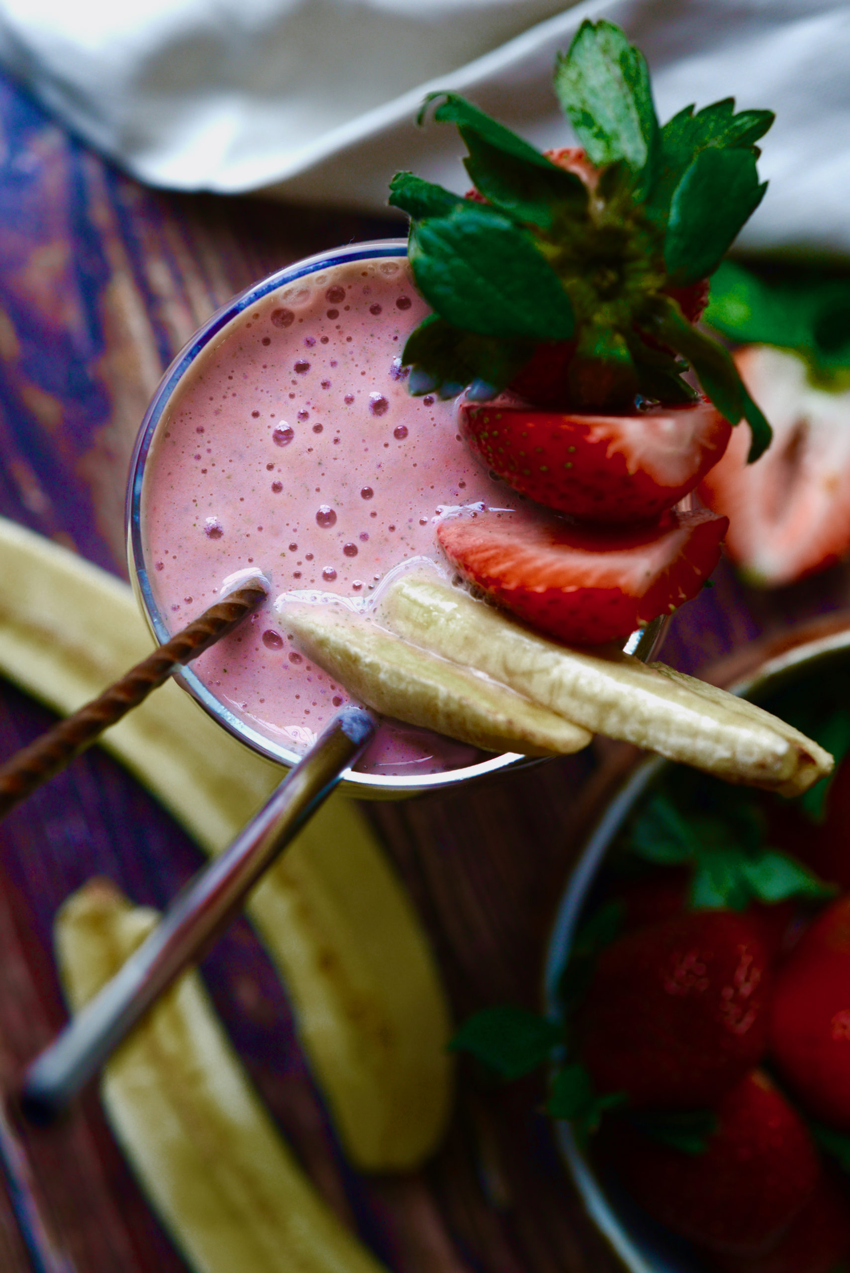 3-ingredient strawberry banana smoothie, areal shot of smoothie in glass with fruit garnishes, straw, and spoon
