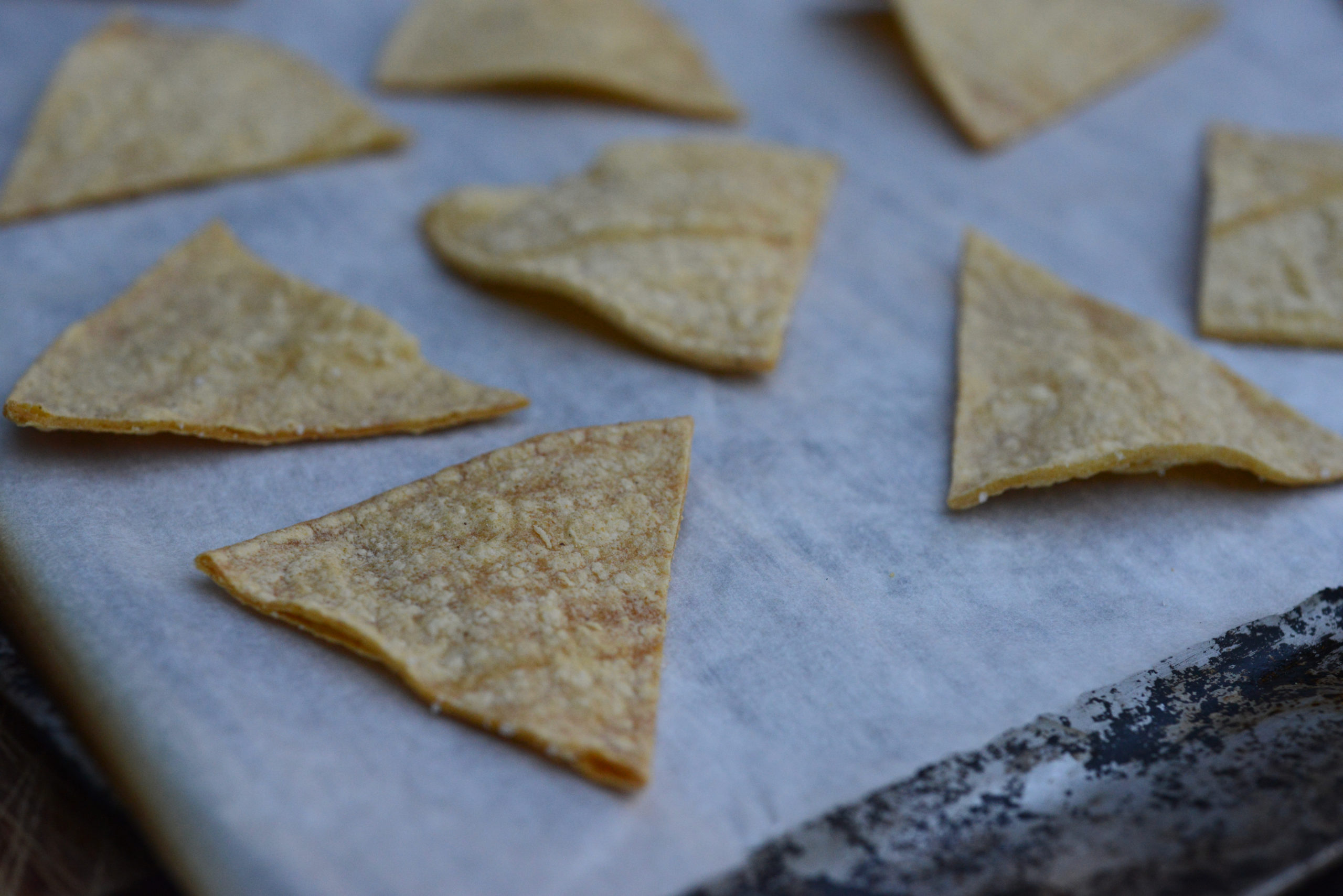 closeup of freshly baked tortilla chips on baking sheet