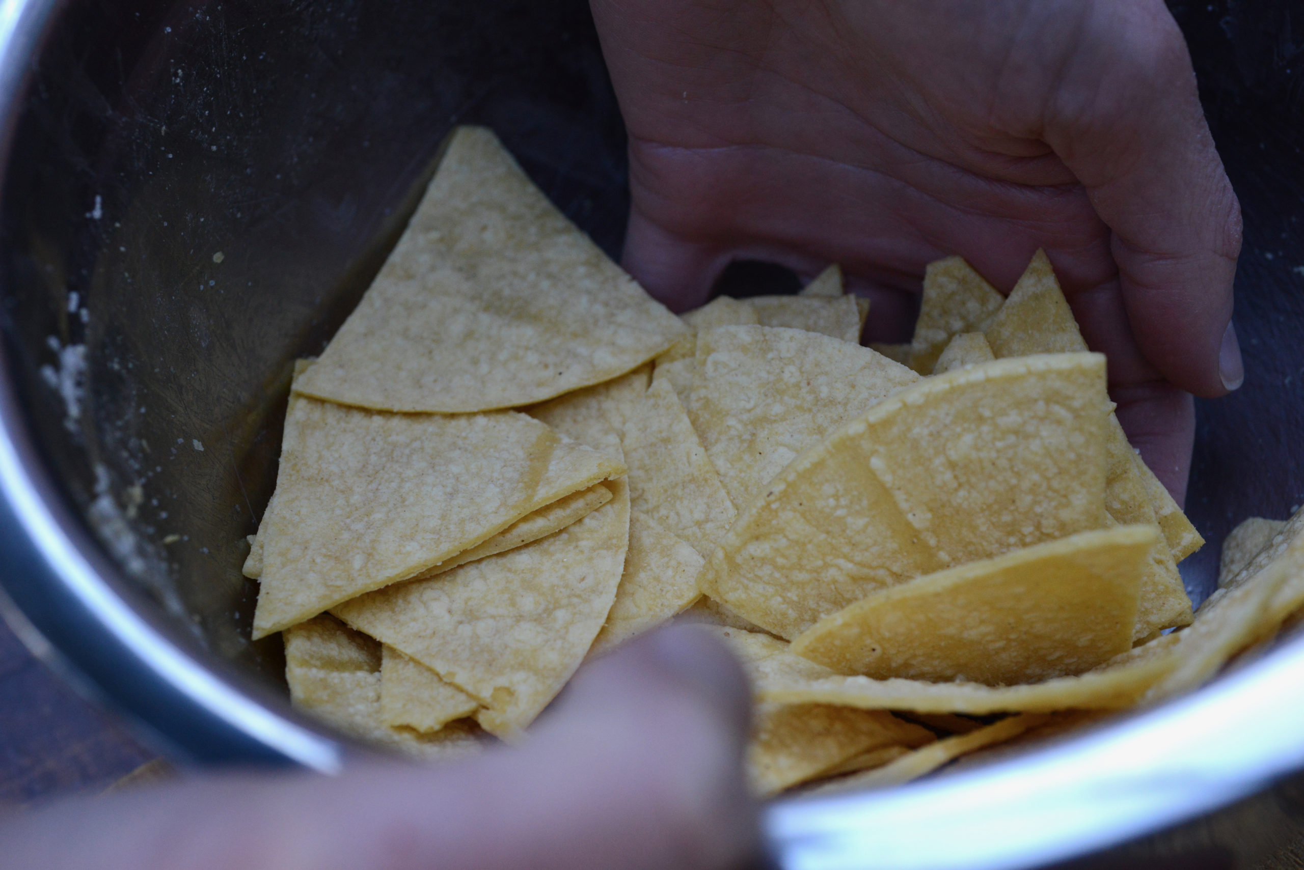 hands tossing tortilla wedges with salt and water in bowl