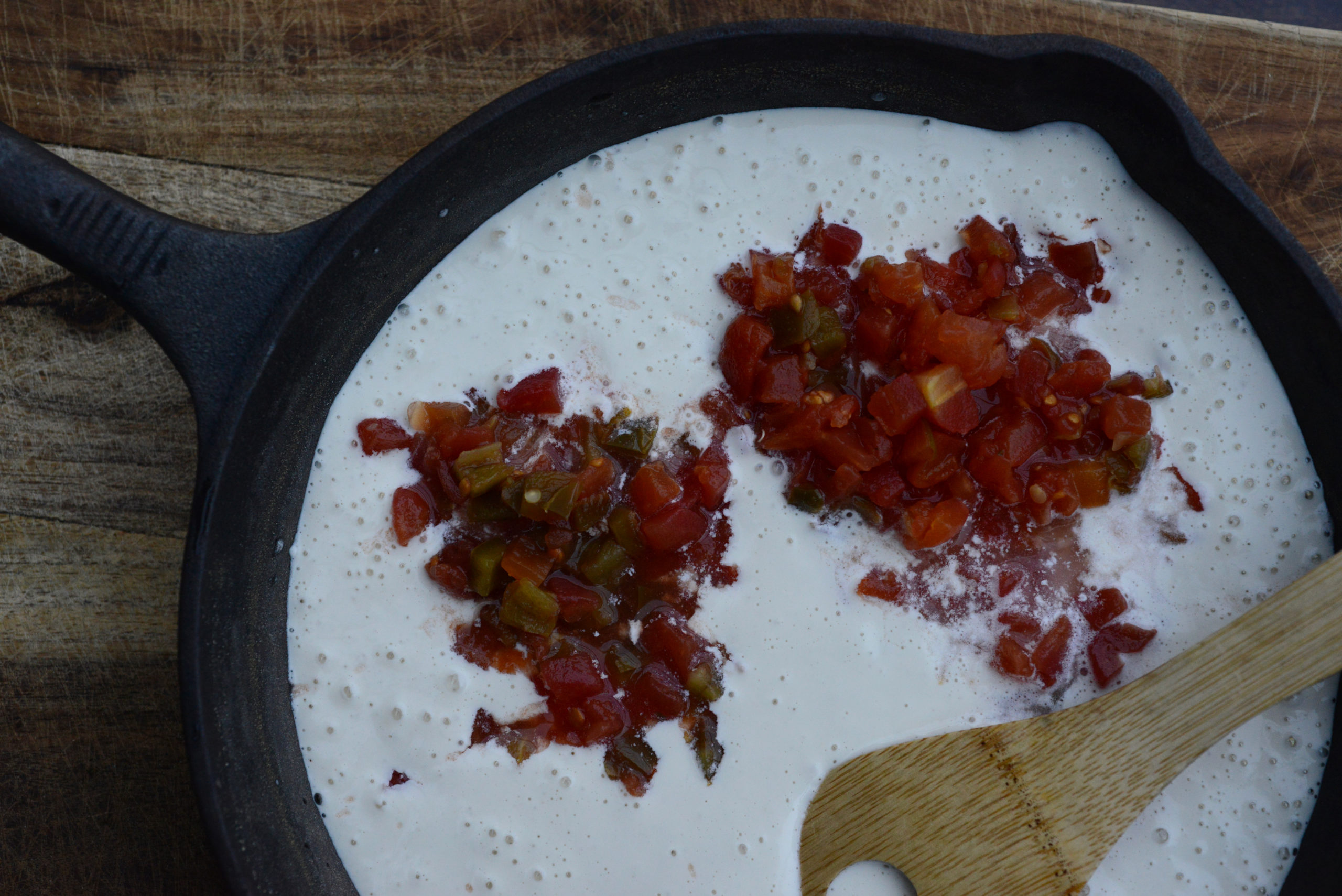 areal shot of canned diced tomatoes with green chilis being added to queso mixture in cast iron skillet