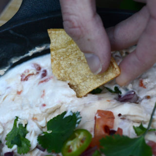 hand dipping homemade tortilla chip into garnished queso dip