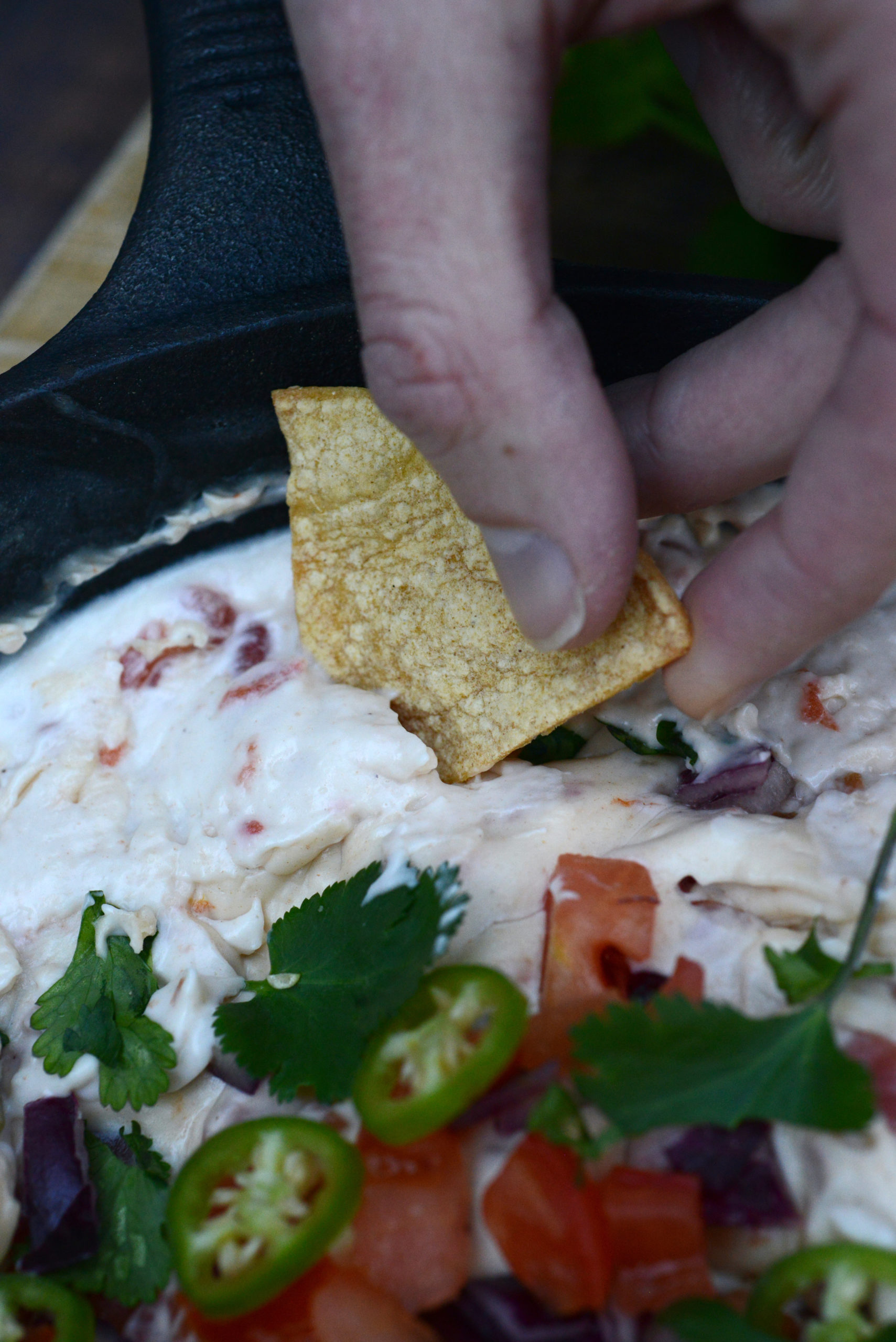 closeup of homemade tortilla chip dipping into garnished queso dip