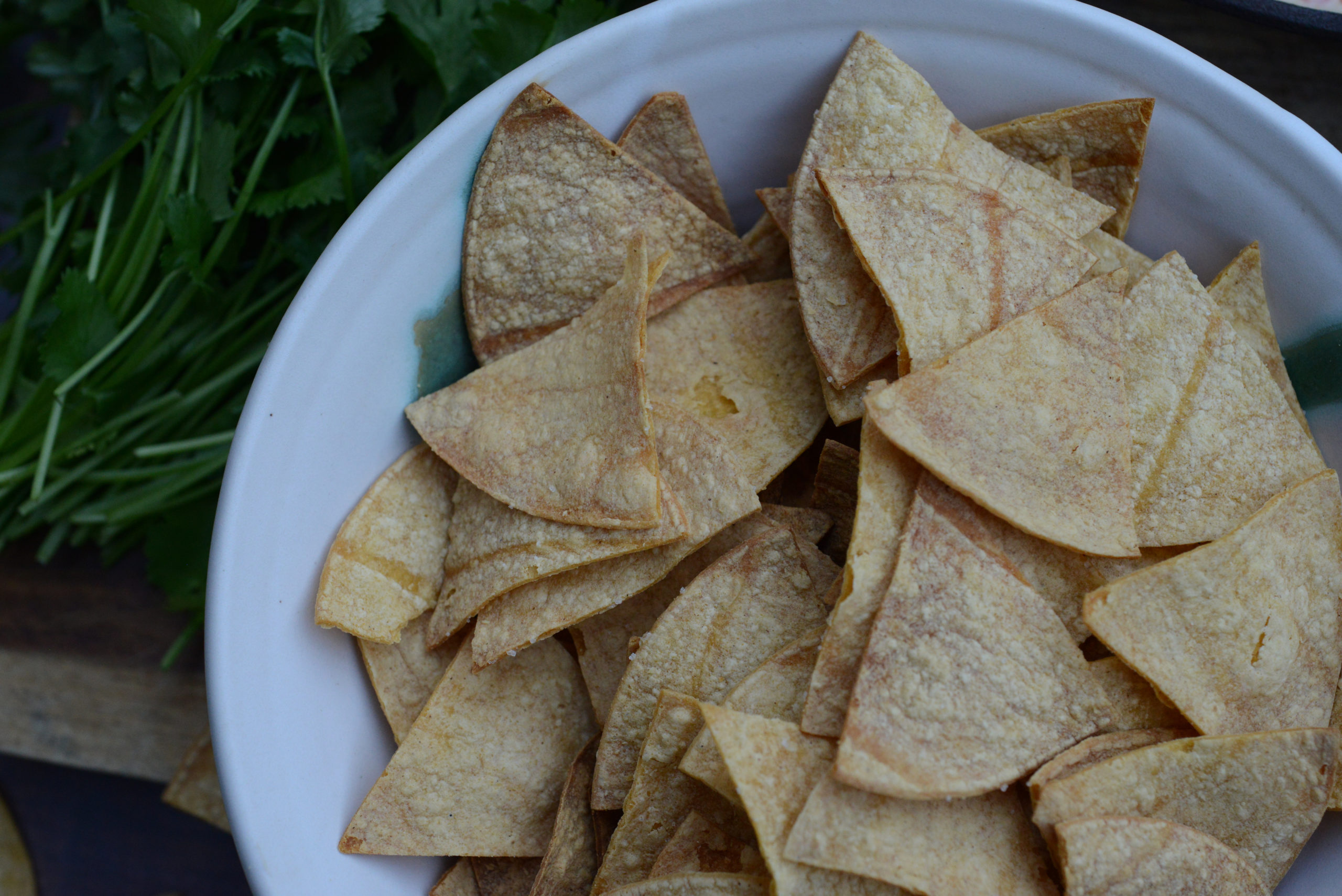 areal view of bowl of homemade oil-free oven-baked tortilla chips in bowl next to cilantro