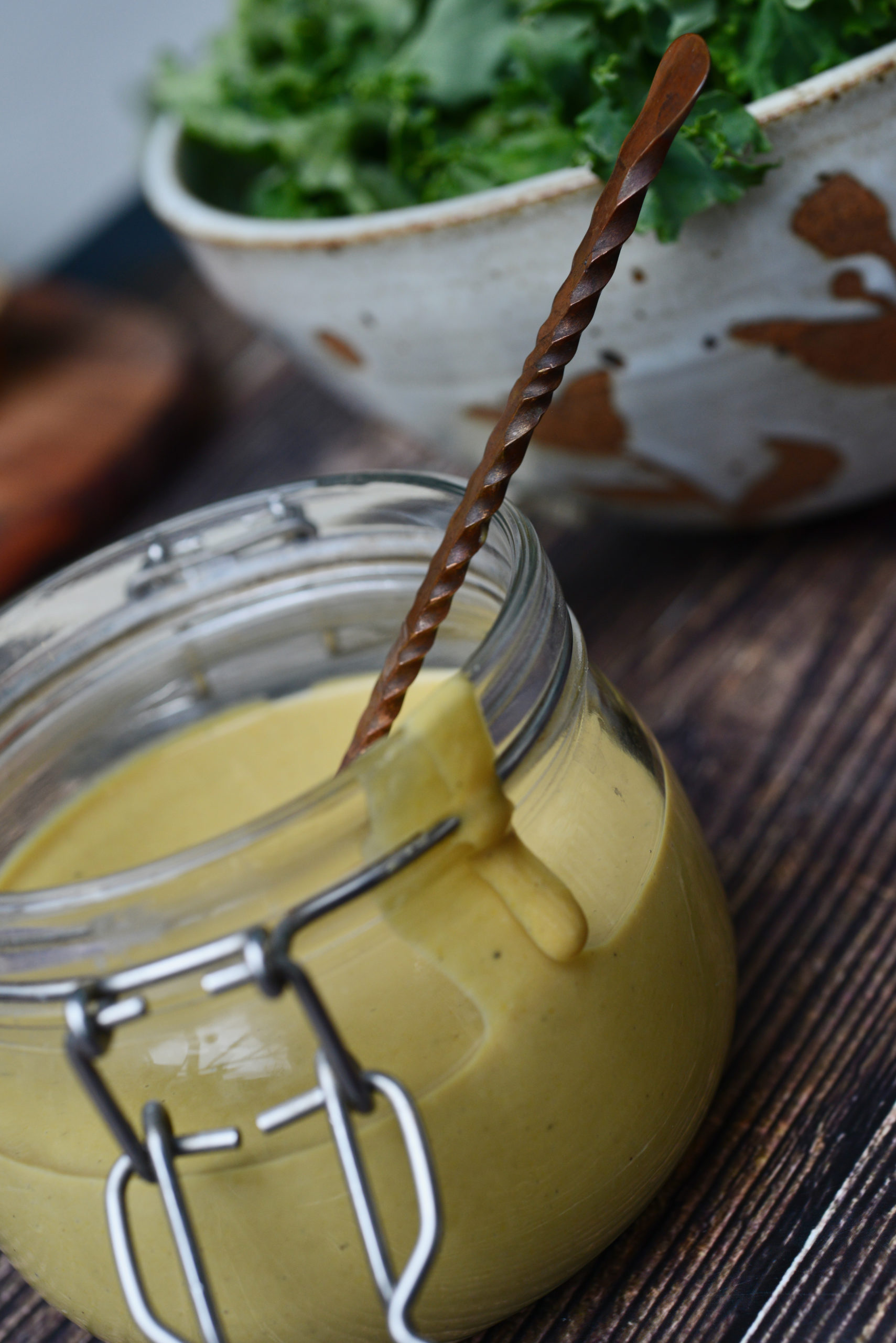 Honeyless Honey Mustard Vegan Dressing in jar with spoon next to white bowl with kale