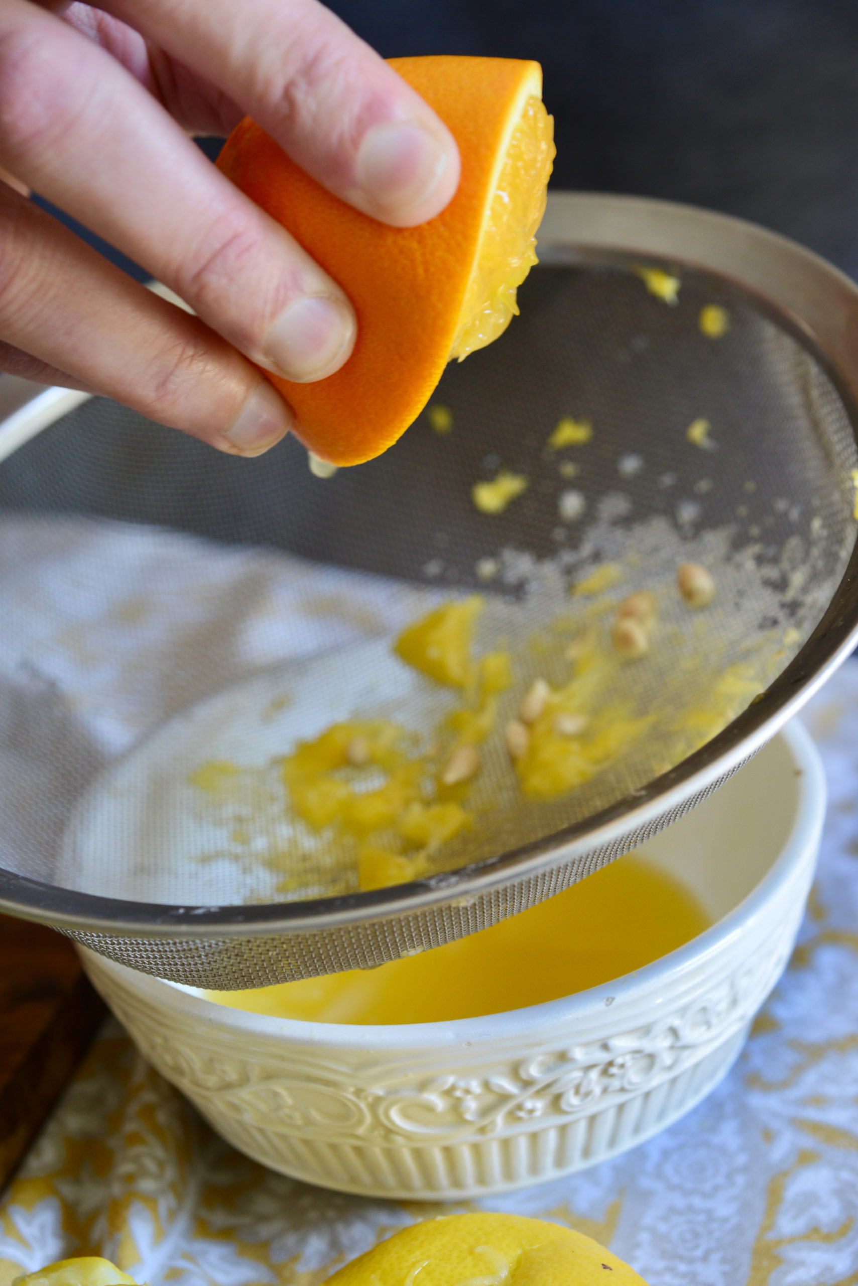 closeup of hand squeezing fresh orange juice into sieve over bowl to collect seeds