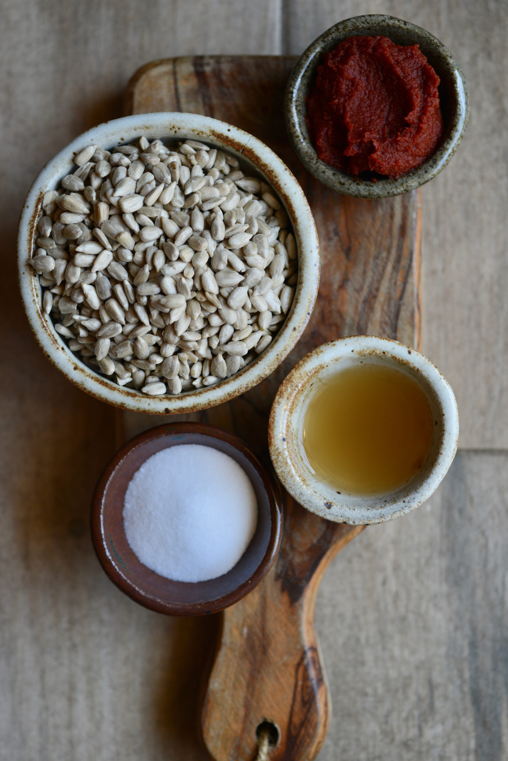 Ingredients for Creamy Plant-Based Mac 'n' Cheese on small wooden board - sunflower seeds, tomato paste, apple cider vinegar, and salt