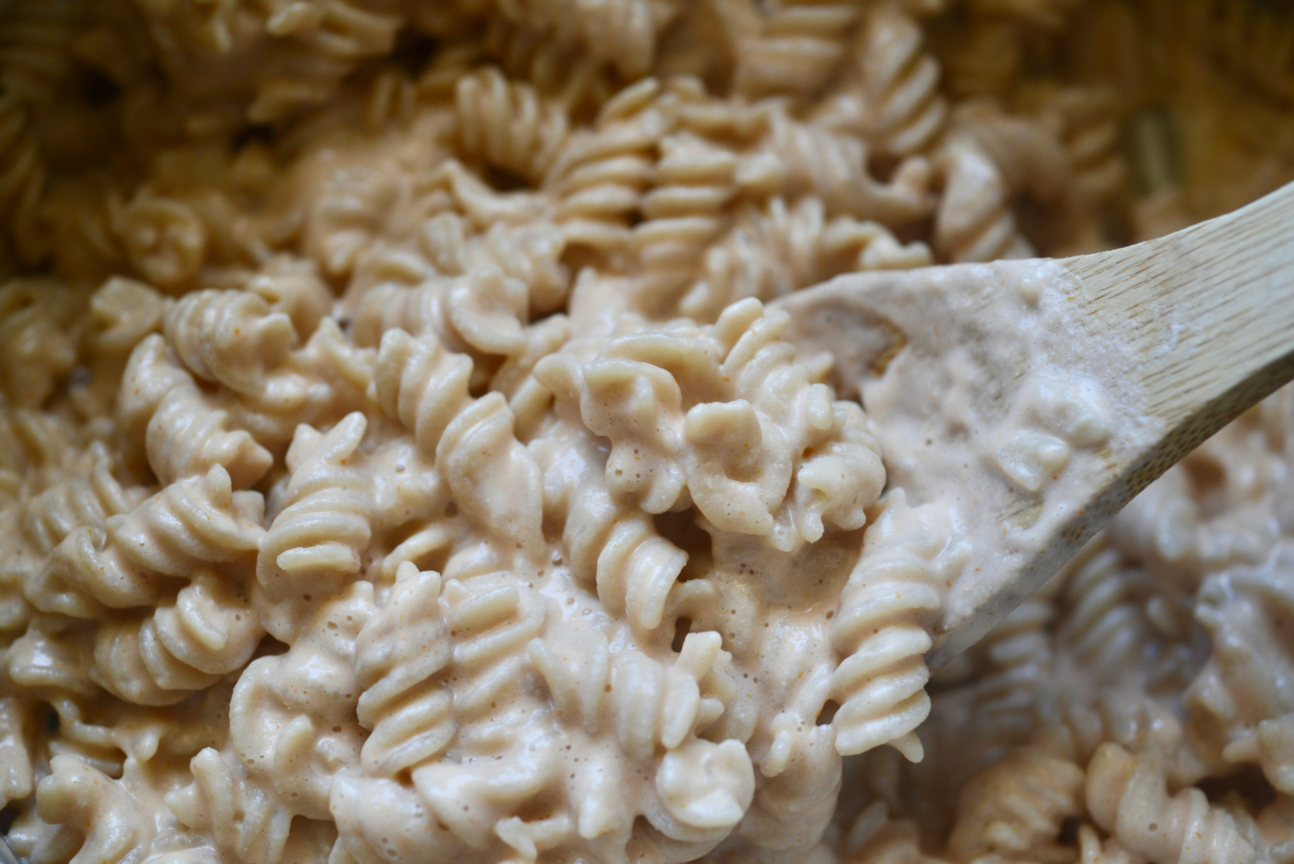 closeup of Creamy Plant-Based Mac 'n' Cheese being stirred with wooden spoon